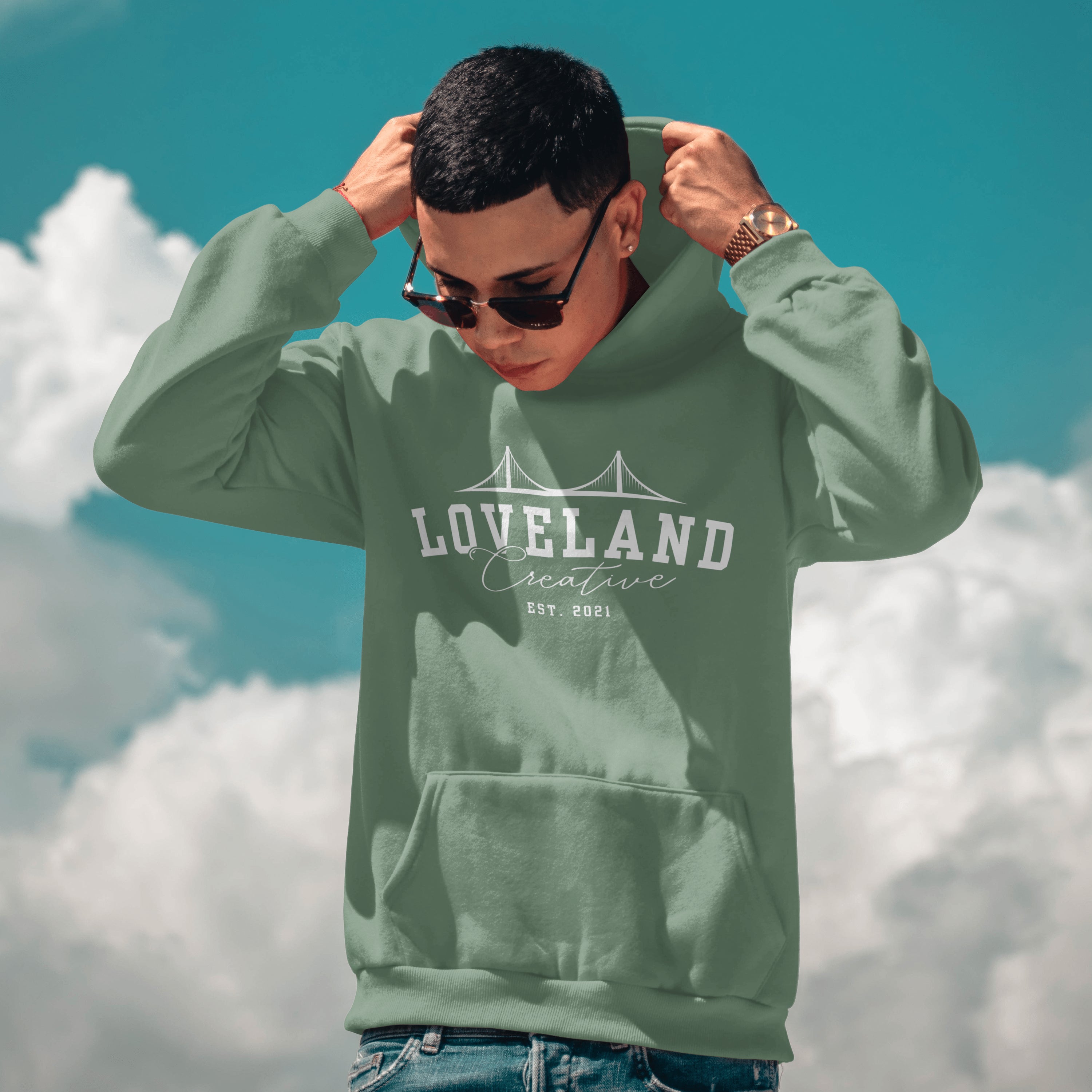 Person wearing a green hoodie with 'Loveland Creative' text against a blue sky with clouds